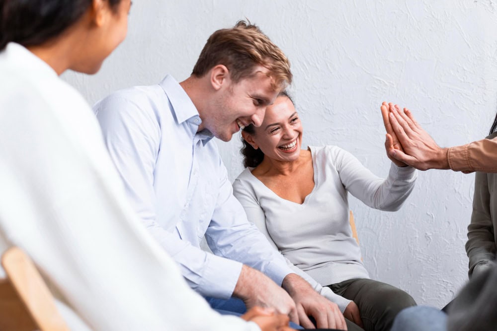 People smiling and greeting one another during a group therapy session for co-occurring PTSD treatment in Massachusetts.