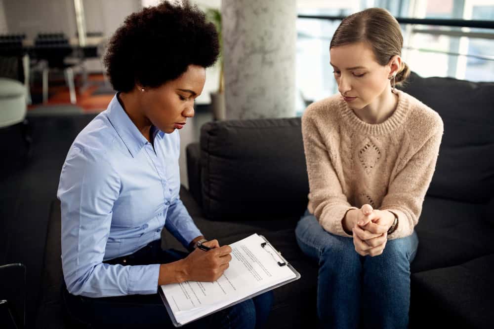 African American therapist taking notes during a patient session as part of women's rehab in Massachusetts at Brook Recovery Centers.