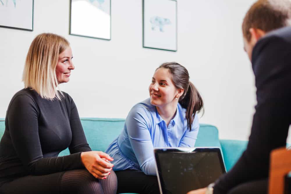 Women sitting together on a couch and smiling during dual diagnosis ADHD treatment in Massachusetts.