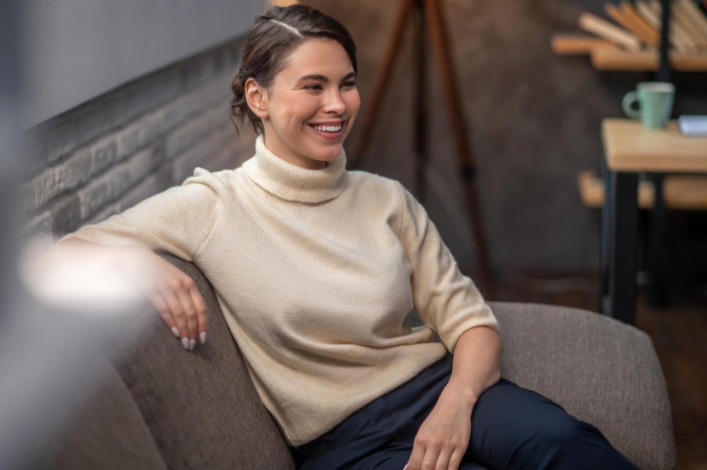 Woman smiling while sitting on a sofa during addiction treatment in Hingham, MA.