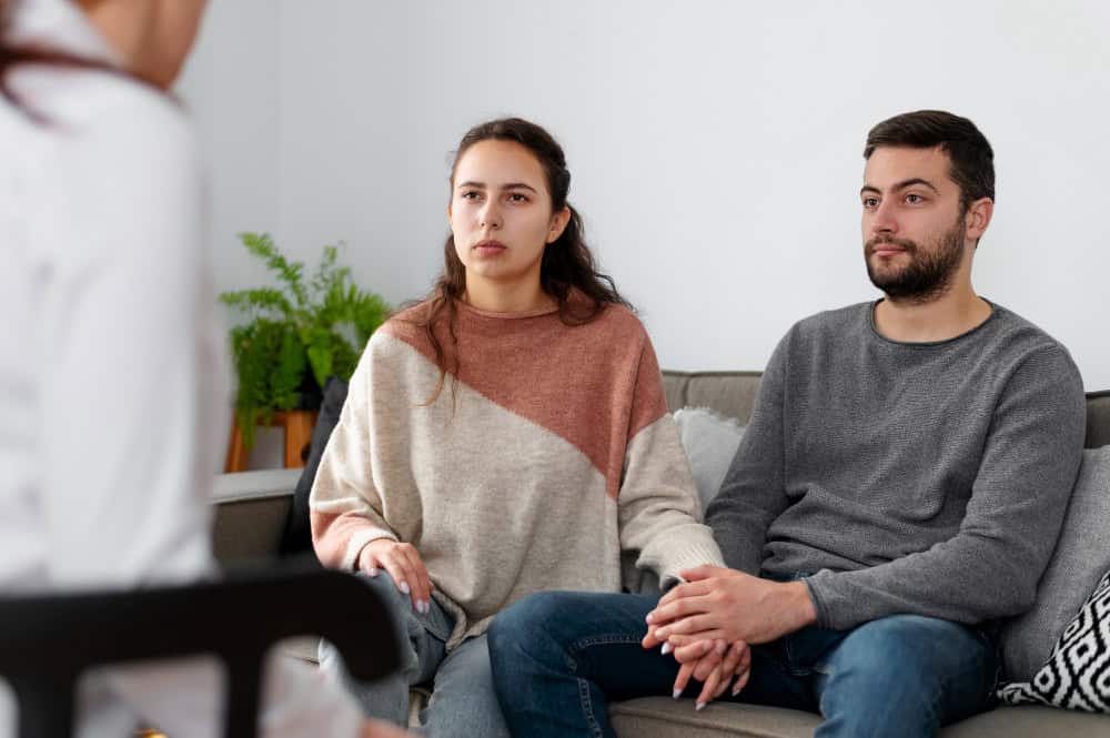 Man and woman holding hands while speaking with their therapist about recovery and relapse.