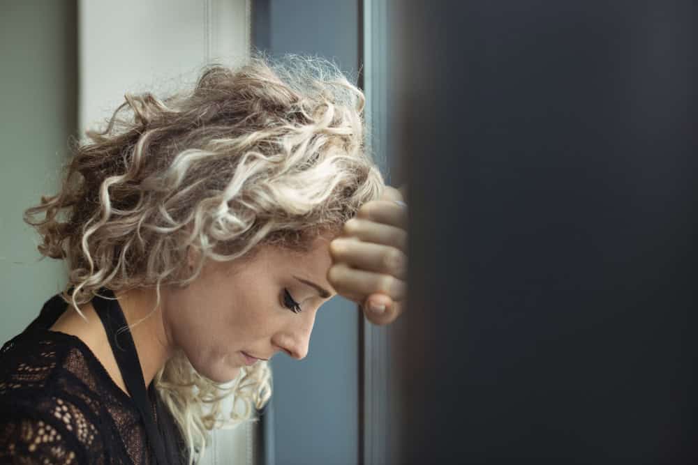 Woman feeling distressed and leaning against a window while seeking BPD and addiction treatment in Massachusetts.